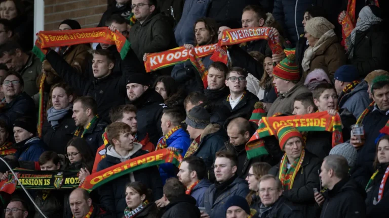 Collectieve supporters op een voetbaltribune met rood-geel-groene sjaals.