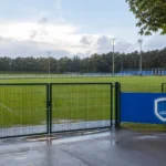 Leeg afgesloten voetbalveld met een KRC Genk-bord langs de zijlijn.