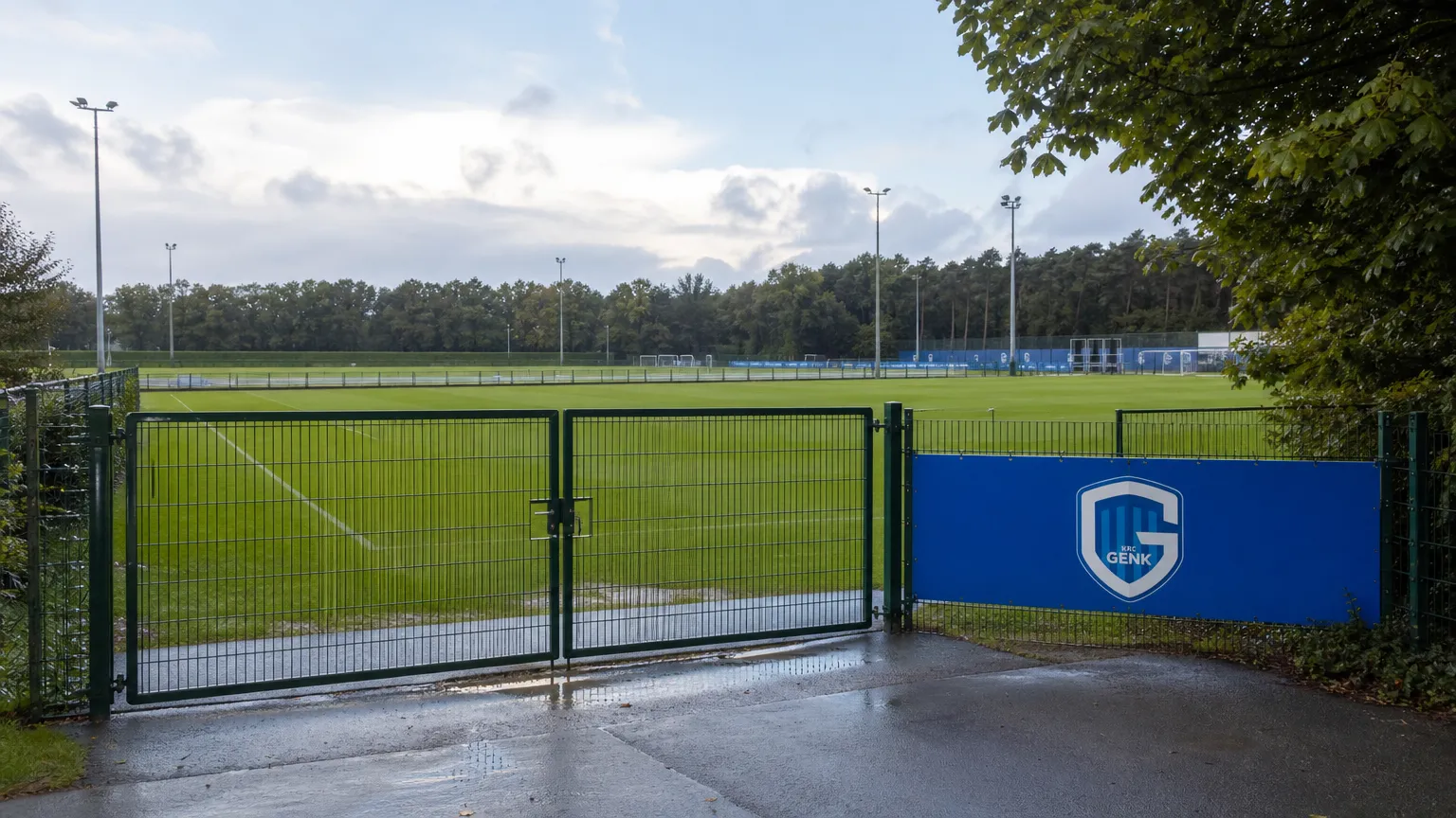Leeg afgesloten voetbalveld met een KRC Genk-bord langs de zijlijn.