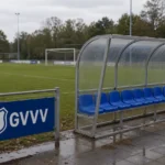 Een lege technische zone langs een amateurvoetbalveld met een vast GVVV-clubbord.