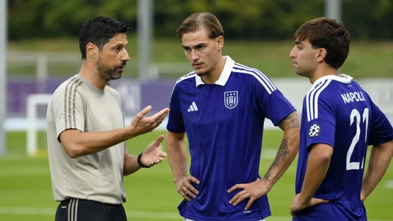 Een trainer geeft op het oefenveld aanwijzingen aan voetballers in paarse shirts.