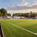 FC Gullegem in het rood en wit bij het compacte Poezelhoek Stadion, met speelveld en hoofdtribune als herkenbare dorpssetting.