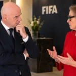 Twee FIFA-officials in gesprek in een formele vergaderruimte.