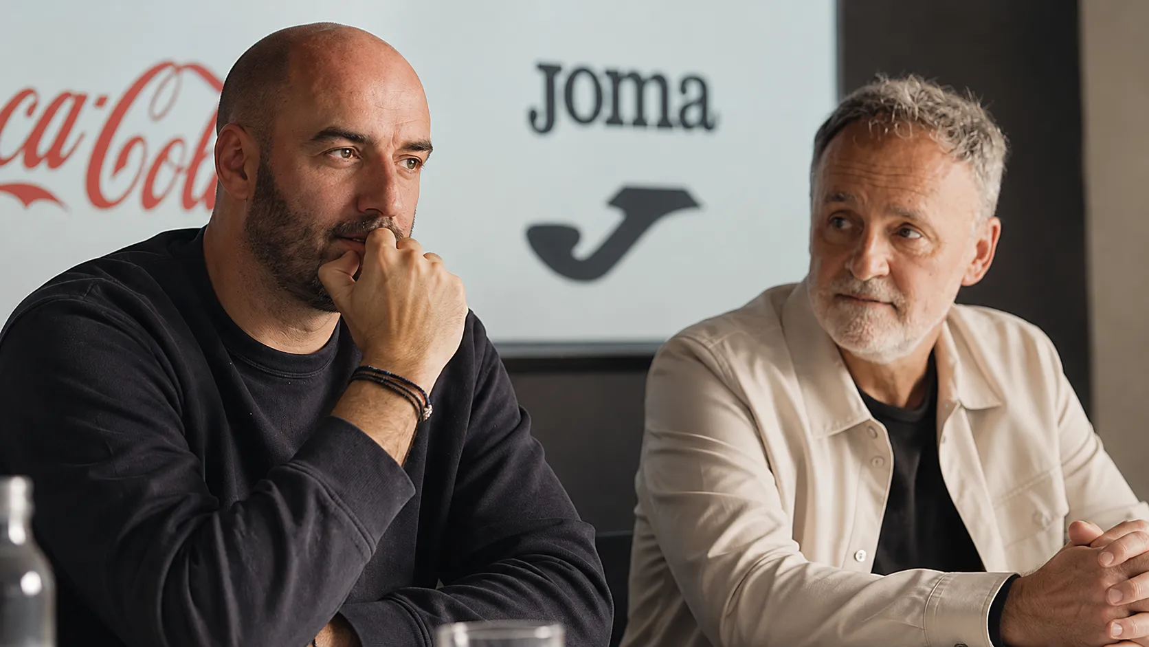 Twee niet-spelende clubmedewerkers in een rustige mediaruimte.