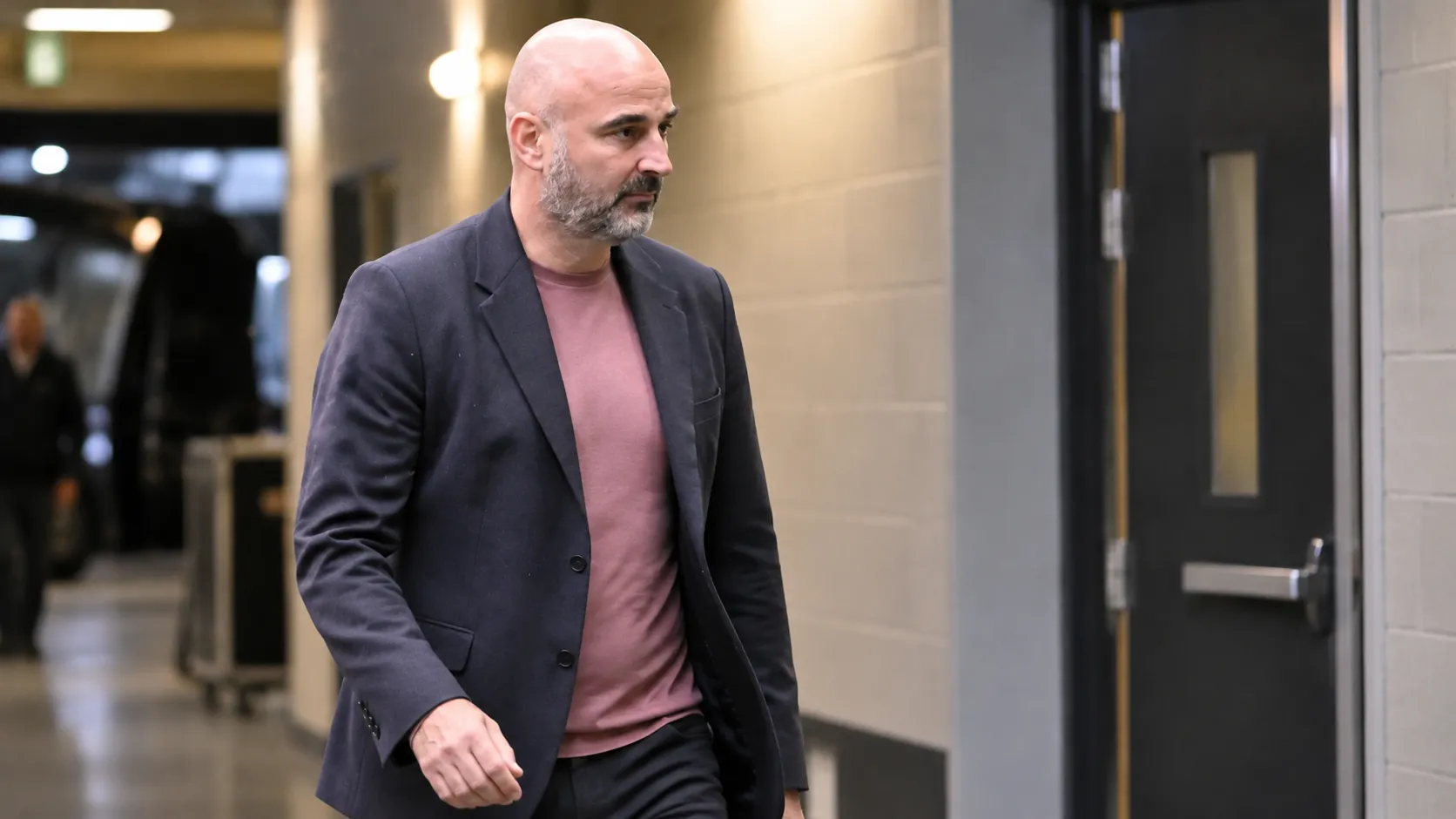 Een niet-spelende clubvertegenwoordiger in donker colbert in een stadionomgeving.