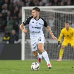 Ryan Merlen van STVV in actie in een wit-zwart tenue op het voetbalveld.