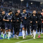 Een groep spelers en stafleden van Olympique Marseille in donkere clubkleding tijdens de warming-up.