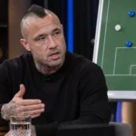 Radja Nainggolan aan tafel in een voetbalstudio met een KAA Gent-tactiekbord op de achtergrond.