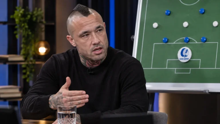 Radja Nainggolan aan tafel in een voetbalstudio met een KAA Gent-tactiekbord op de achtergrond.