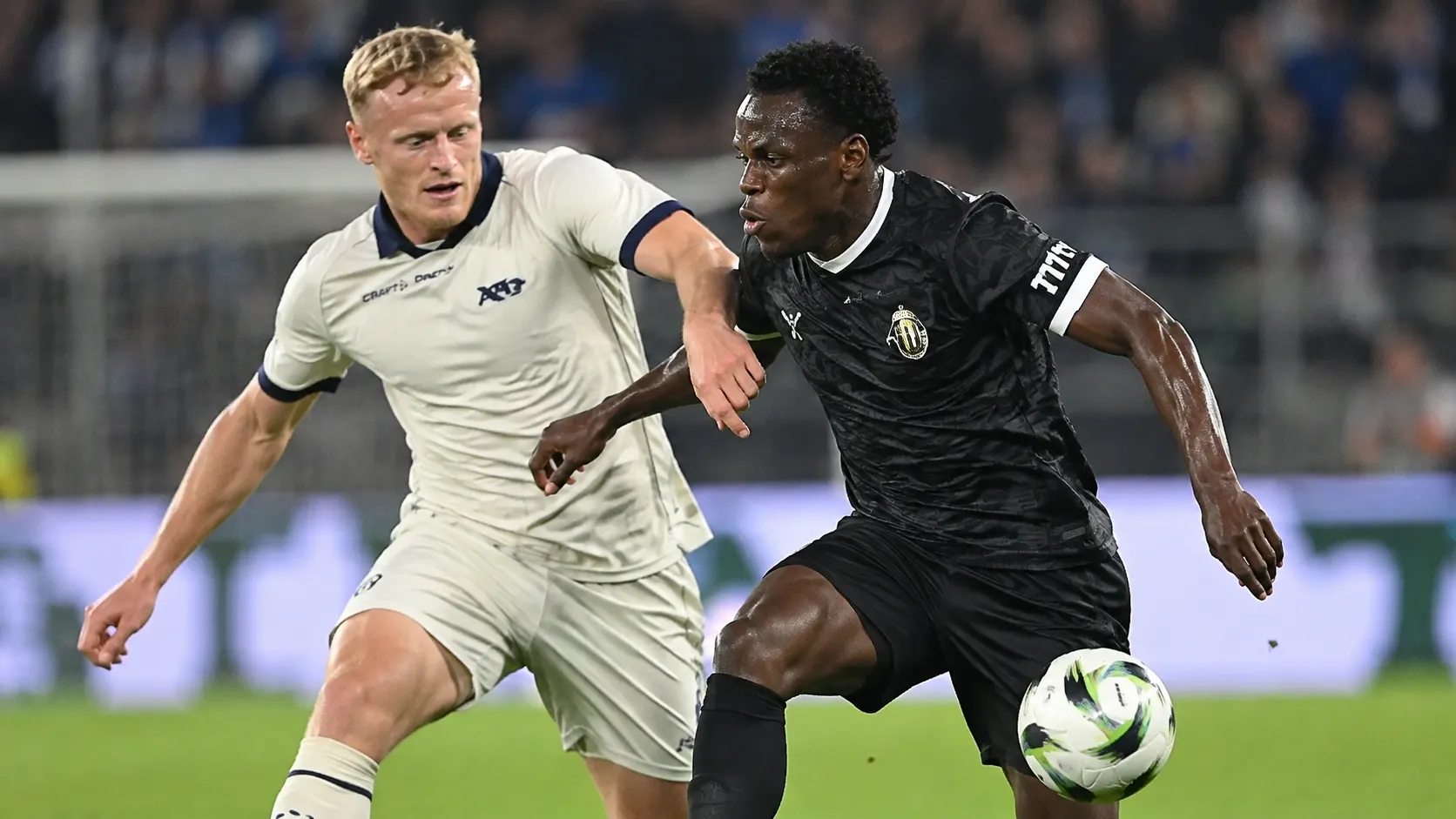 Twee voetballers in duel tijdens een wedstrijd, met een speler in zwart op de voorgrond.