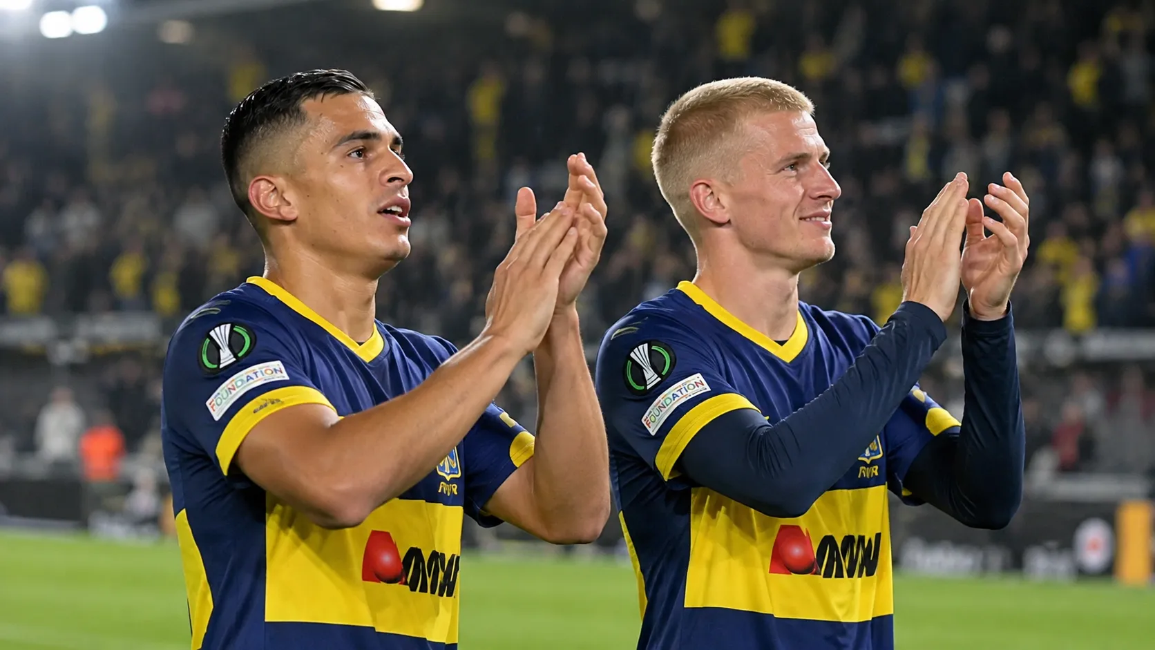 Twee voetballers in donkerblauw-geel tenue applaudisseren na een Europese wedstrijd.
