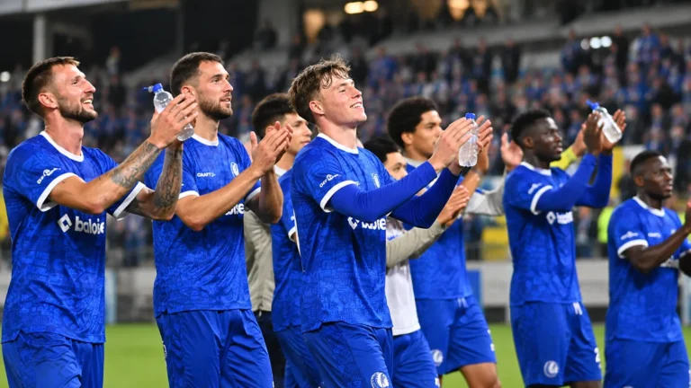 Een groep voetballers in blauwe wedstrijdshirts applaudisseert na afloop richting de tribunes.