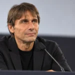 Antonio Conte in neutrale donkere kleding op een voetbalconferentie.