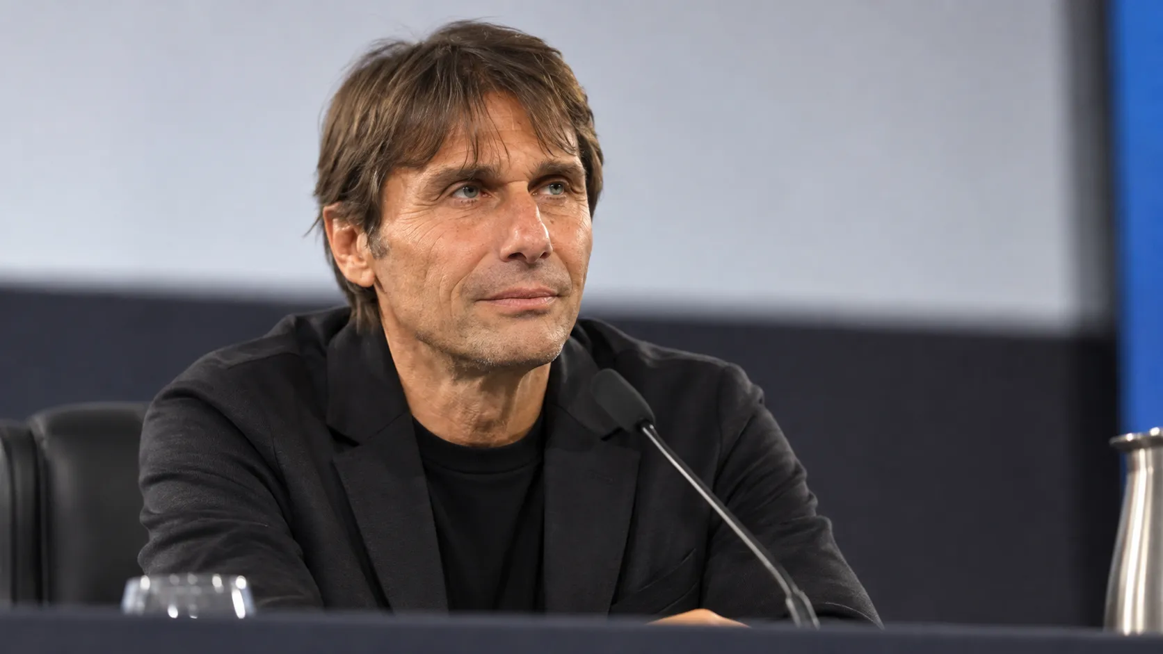 Antonio Conte in neutrale donkere kleding op een voetbalconferentie.