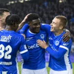 Een groep voetballers in blauwe shirts viert samen op het veld.