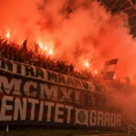 Groep Hajduk Split-supporters met spandoeken in een rood-oranje rookgordijn op de tribune.