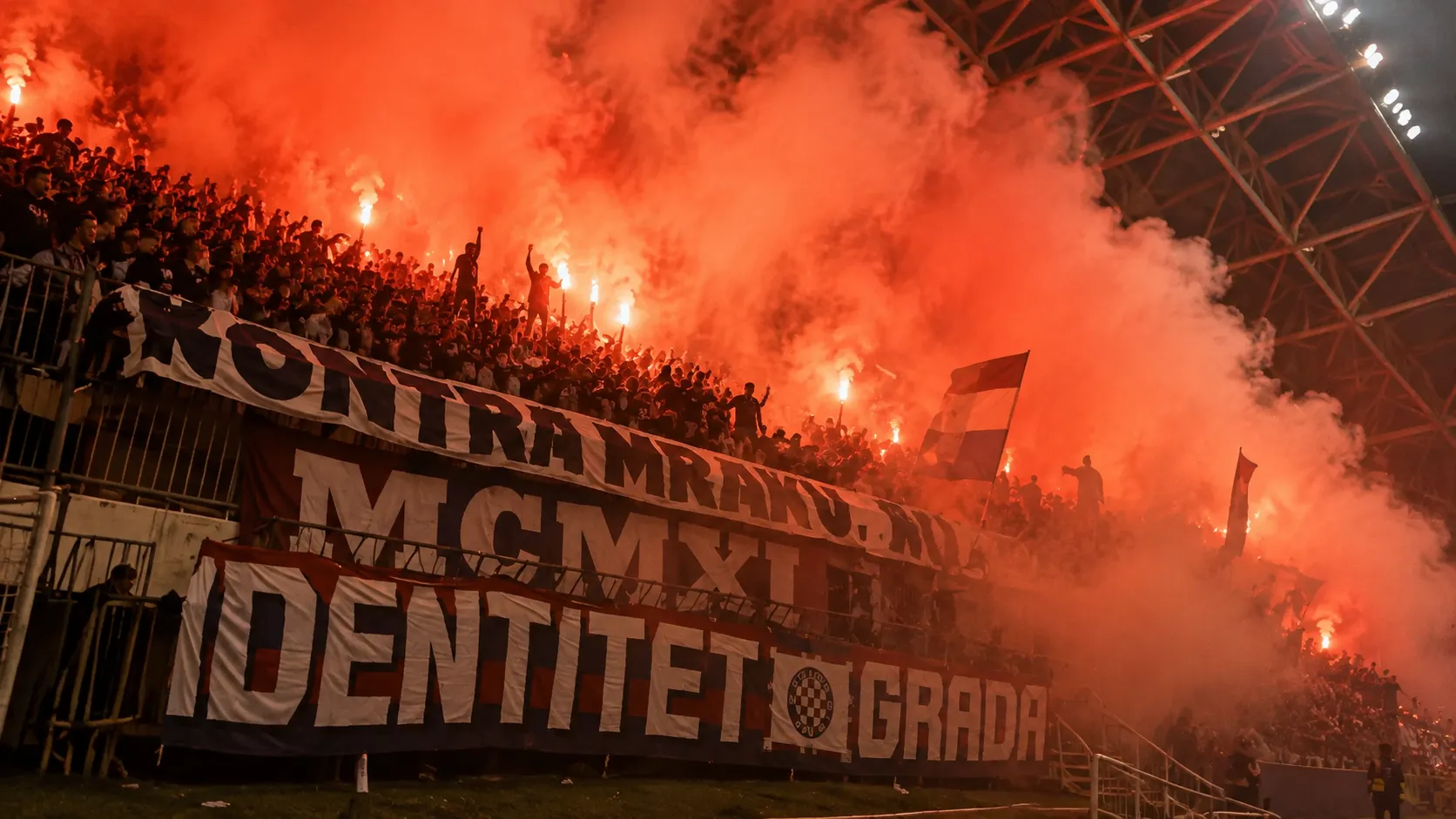 Groep Hajduk Split-supporters met spandoeken in een rood-oranje rookgordijn op de tribune.