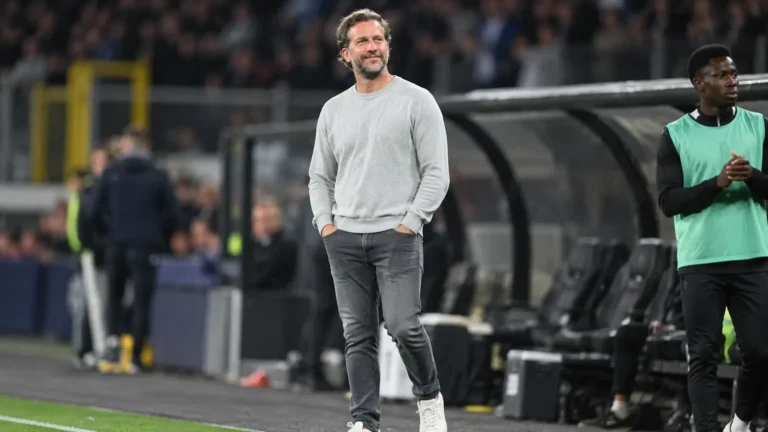 Rik De Mil in een grijze trui langs de zijlijn van een stadion.