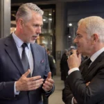 Twee voetbalbestuurders in donkere pakken in gesprek bij een stadioningang.