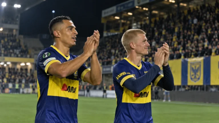 Twee STVV-spelers in blauw-geel tenue applaudisseren na de wedstrijd in het stadion.