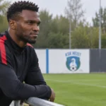 Obbi Oulare in neutrale sportkleding naast het trainingsveld van KSK Heist.