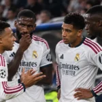 Vier Real Madrid-spelers in witte shirts staan samen op het veld tijdens een wedstrijdonderbreking.