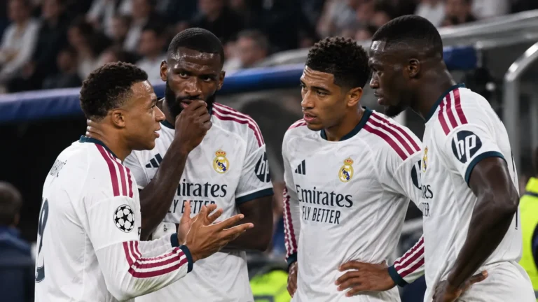 Vier Real Madrid-spelers in witte shirts staan samen op het veld tijdens een wedstrijdonderbreking.