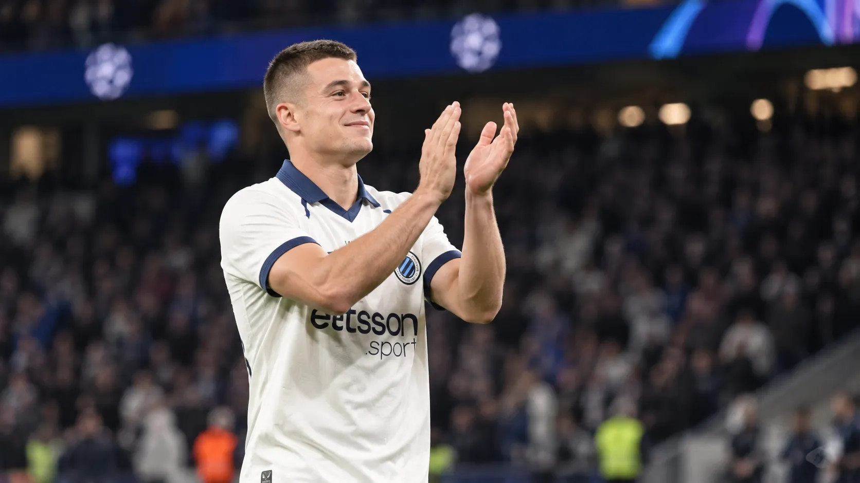 Nicolò Tresoldi in het witte shirt van Club Brugge terwijl hij na een wedstrijd naar de tribunes applaudisseert.