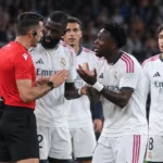 Een groep Real Madrid-spelers bespreekt een beslissing met een scheidsrechter langs het veld.