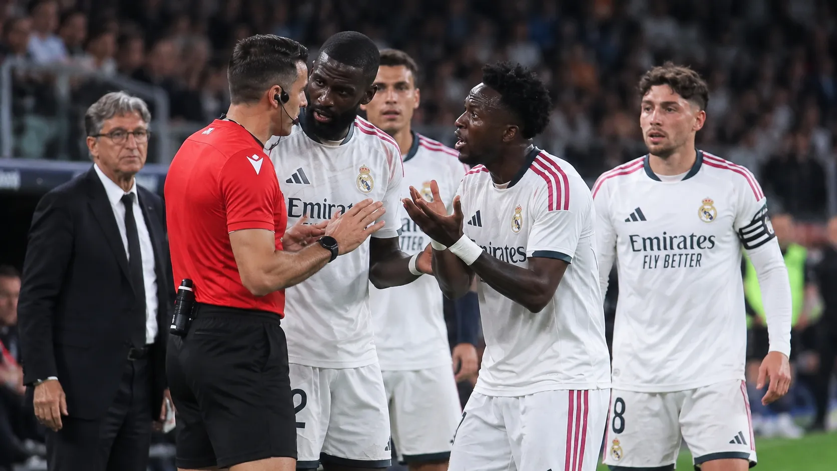 Een groep Real Madrid-spelers bespreekt een beslissing met een scheidsrechter langs het veld.