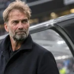 Jürgen Klopp in donkere jas langs de zijlijn van een stadion, met een Duits embleem op het bankpaneel.