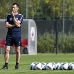 Een staflid van Antwerp in trainingskleding op het trainingsveld met voetballen.