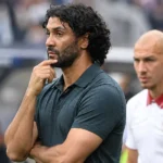 Marvin Compper staat geconcentreerd langs de zijlijn met een speler op de achtergrond.