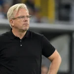 Lars Friis aan de zijlijn van een voetbalstadion in een zwart poloshirt.