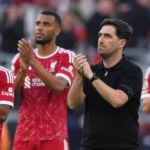 Een staflid en enkele spelers applaudisseren langs de zijlijn van een voetbalstadion.