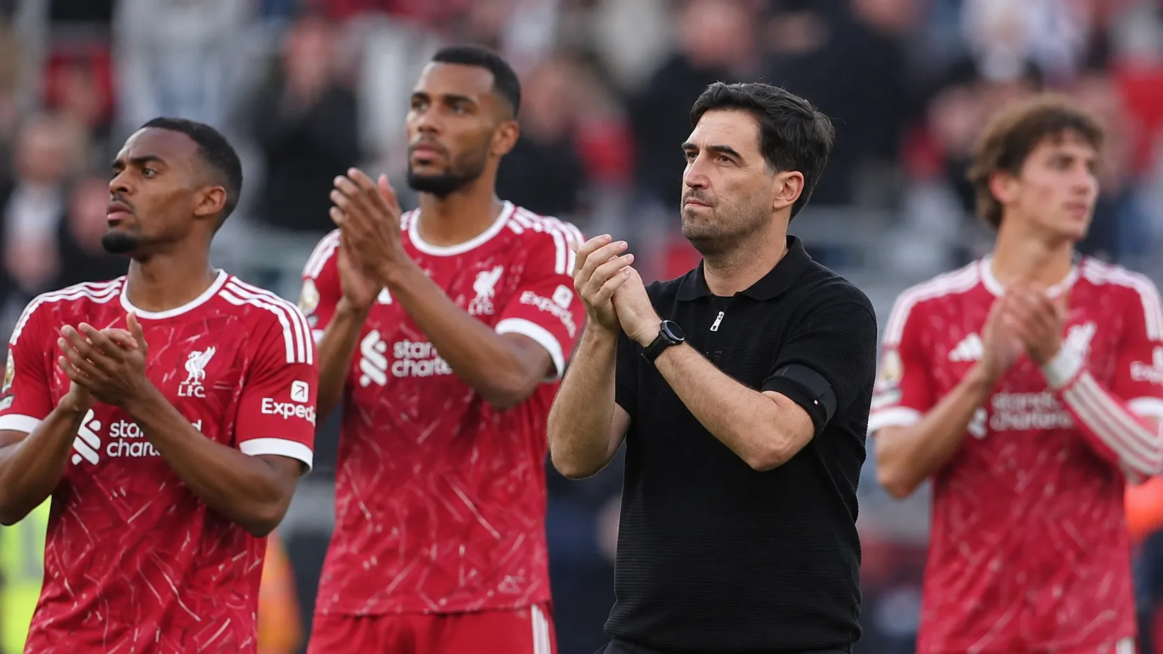 Een staflid en enkele spelers applaudisseren langs de zijlijn van een voetbalstadion.