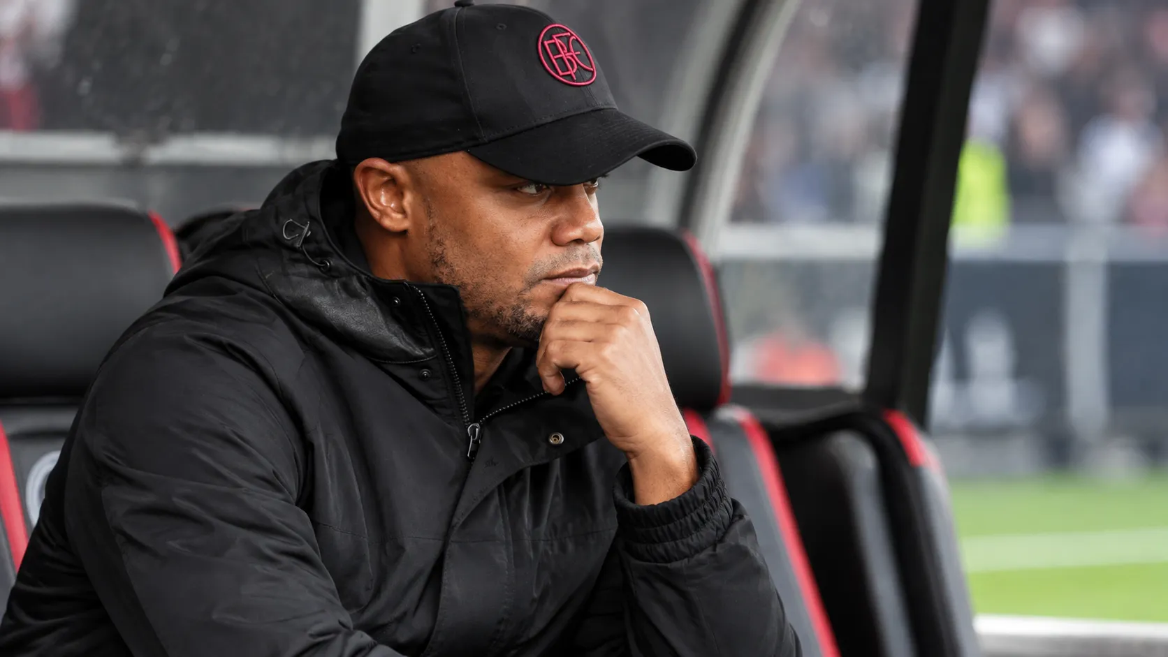 Vincent Kompany zit geconcentreerd in de technische zone langs een voetbalveld.
