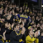 Supporters van Union applaudisseren in de tribune met een blauw-gele sjaal.