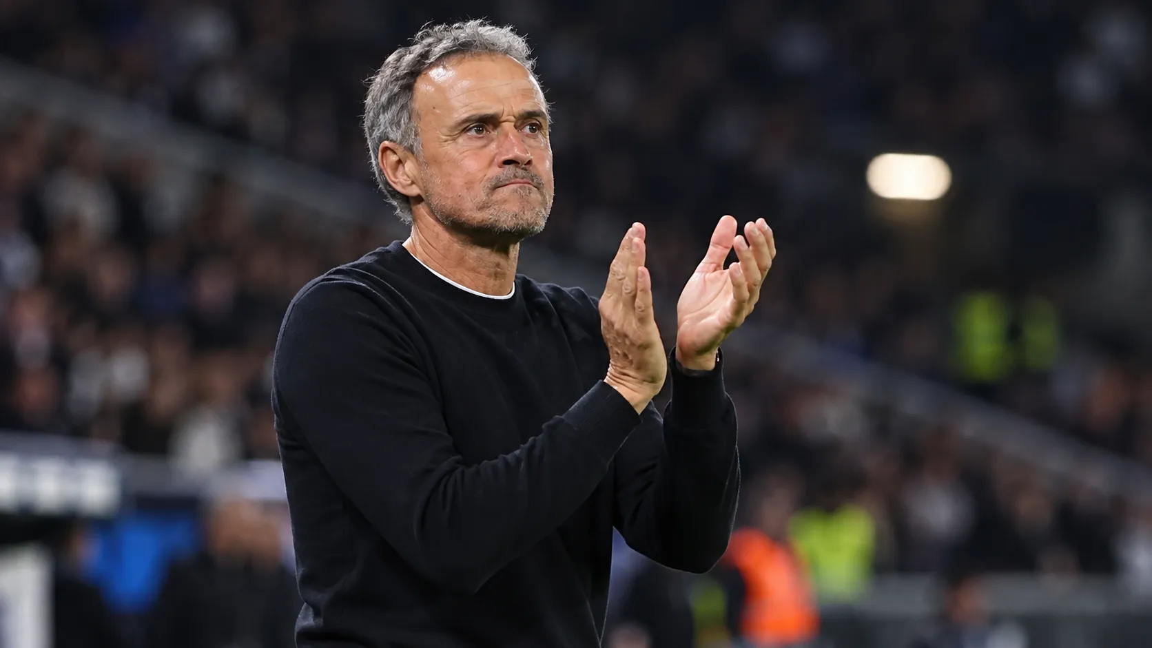 Een PSG-coach applaudisseert langs de zijlijn tijdens een avondwedstrijd.