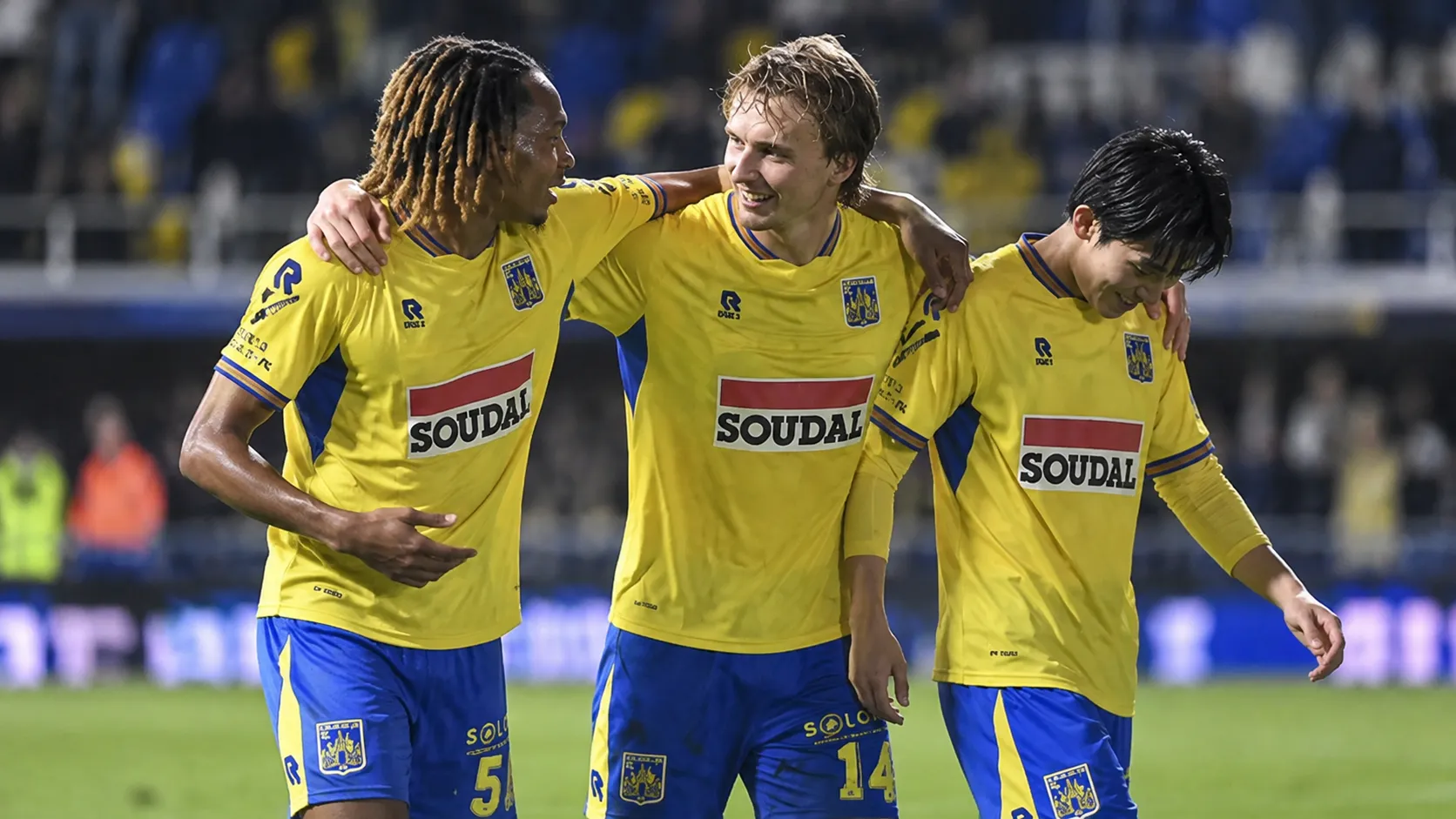 Drie spelers van KVC Westerlo in geel-blauwe wedstrijdkleding vieren samen na een match.