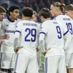 Een groep spelers in witte shirts vormt een kring voor een wedstrijd.