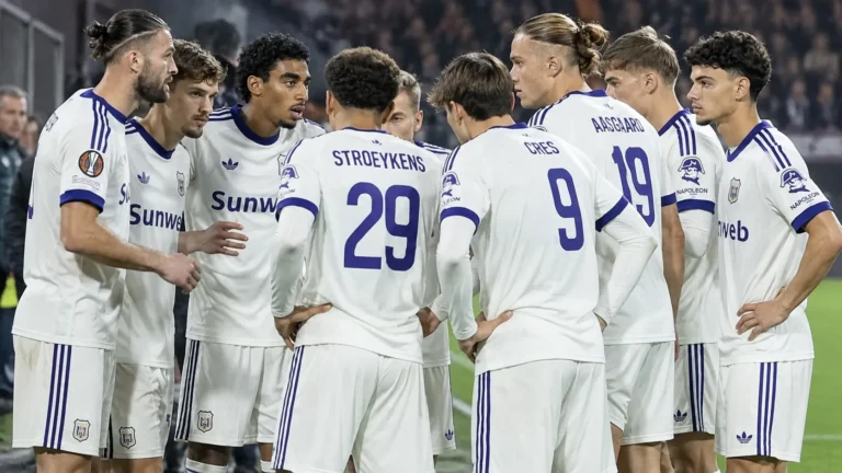 Een groep spelers in witte shirts vormt een kring voor een wedstrijd.