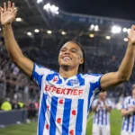 Een speler van sc Heerenveen heft beide armen op in een verlicht stadion.