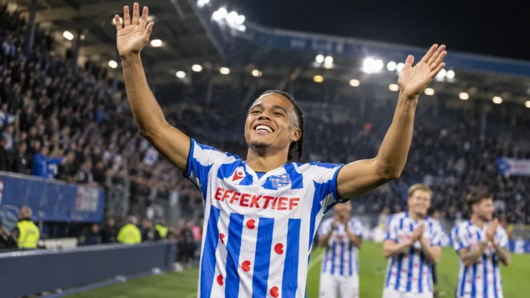 Een speler van sc Heerenveen heft beide armen op in een verlicht stadion.