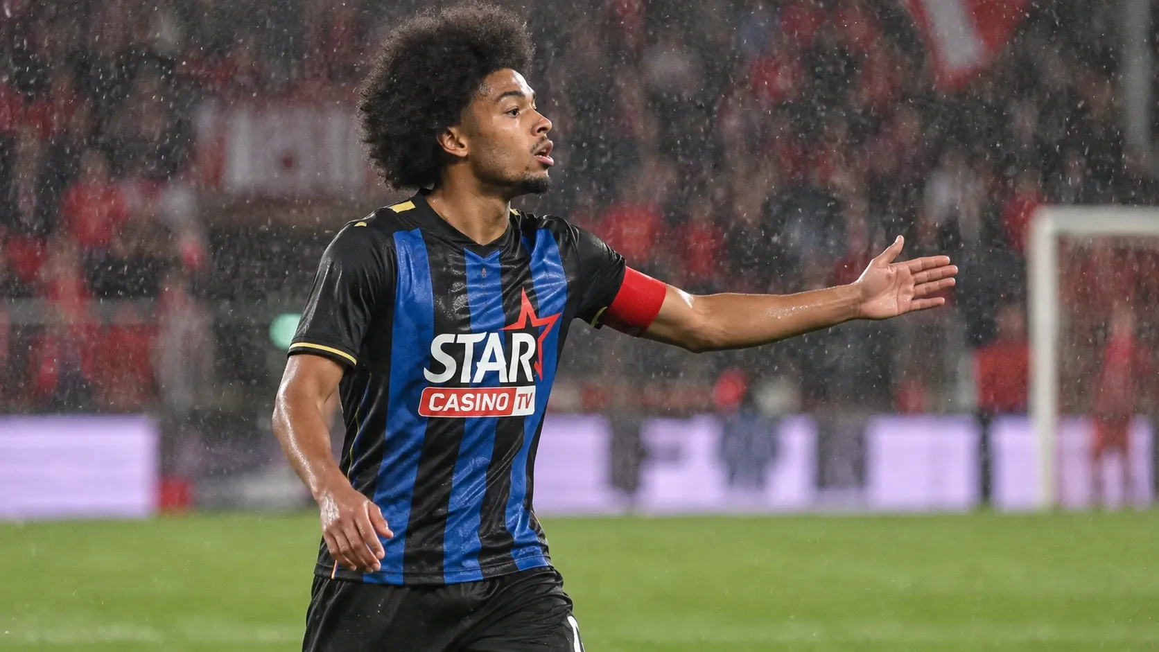 Een speler in een zwart-blauw gestreept tenue tijdens een regenachtige wedstrijd op Sclessin.