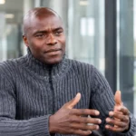 Mbo Mpenza tijdens een interview in een rustige voetbalmediaomgeving.