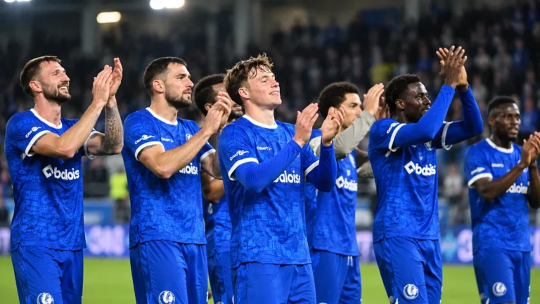 Een groep voetballers in blauwe wedstrijdshirts applaudisseert samen in een stadion.