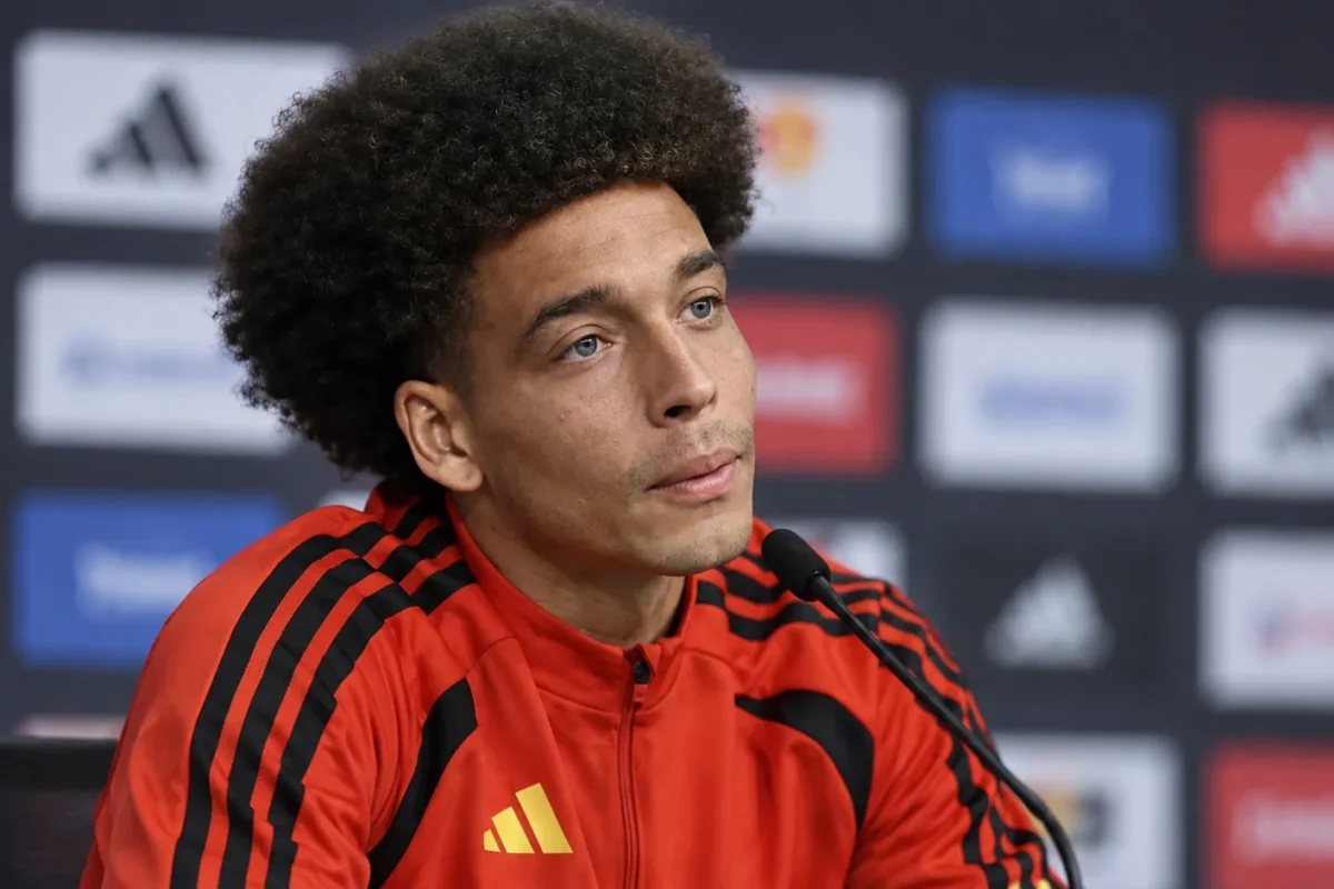 Axel Witsel tijdens een voetbalinterview in een rode sportjas voor een persachtergrond.