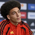 Axel Witsel tijdens een voetbalinterview in een rode sportjas voor een persachtergrond.