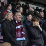 Collectieve groep teleurgestelde Burnley-supporters op de tribune met een Burnley-sjaal.